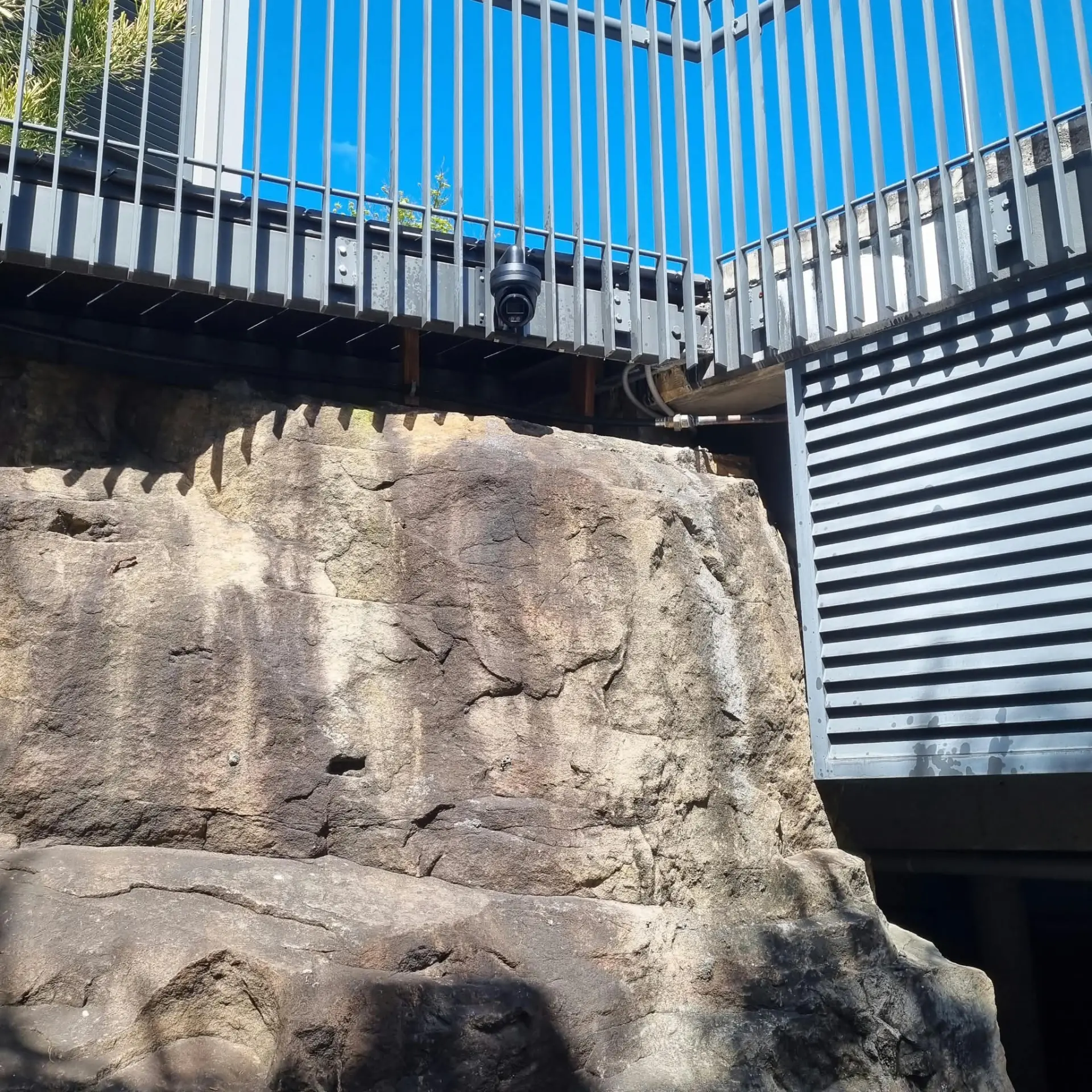 Camera mounted under a balcony railing above a sandstone wall